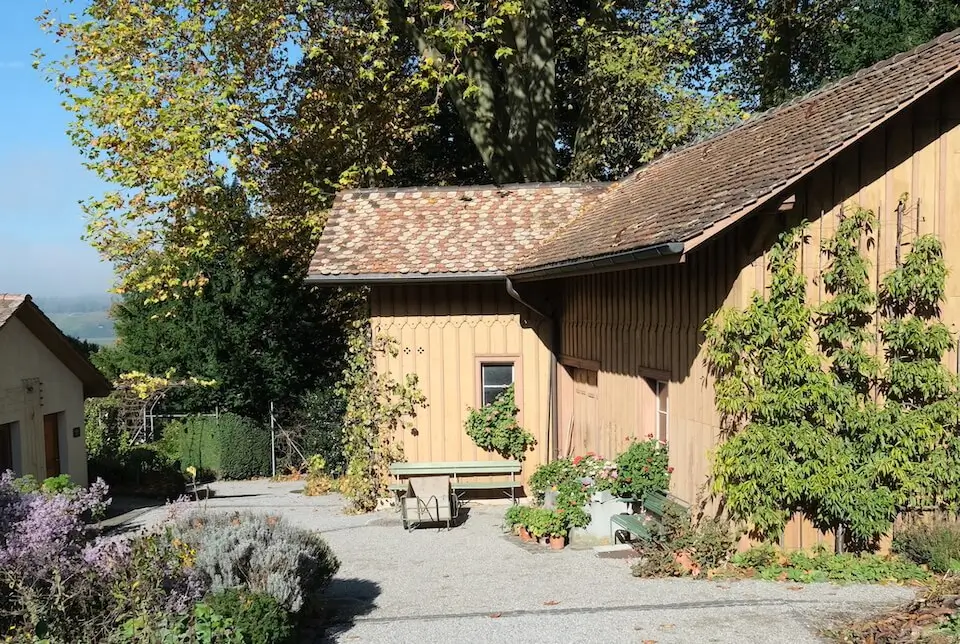 Holzhaus mit verschieden farbigen Biberschwanzziegeln mitten in einem grünen Garten. 
