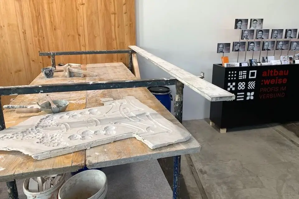 Arbeitstisch mit Gussform für die Erstellung von Stuckaturen. Im Hintergrund Broschürenständer der Altbauweise.